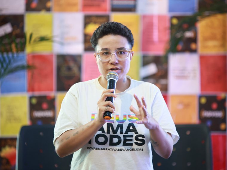 Pessoa ao microfone com camiseta escrita Deus ama todes