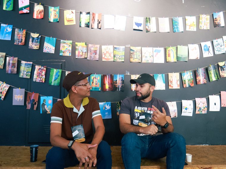 Duas pessoas conversando sentadas diante de um varal de zines