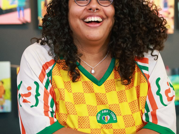 Mulher sorrindo, sentada, com a camisa do Novas